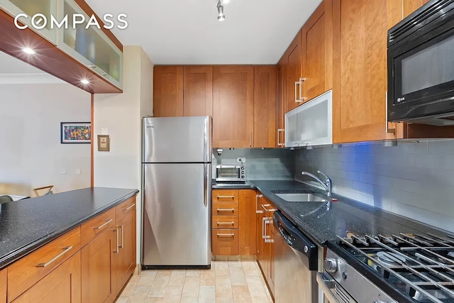 kitchen with dark stone counters, decorative backsplash, brown cabinets, stainless steel appliances, and a sink