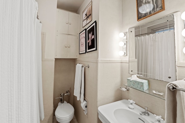 bathroom with a wainscoted wall, tile walls, curtained shower, toilet, and a sink