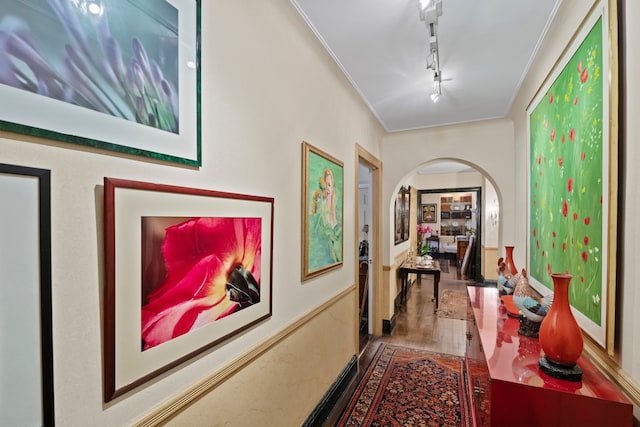 corridor featuring arched walkways, ornamental molding, wood finished floors, and track lighting