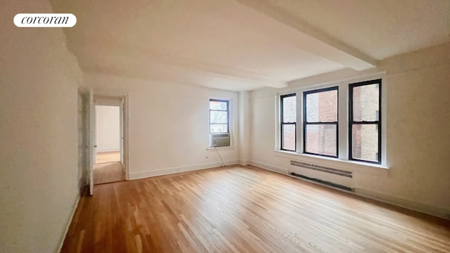 empty room with cooling unit, beam ceiling, radiator, and light wood-type flooring