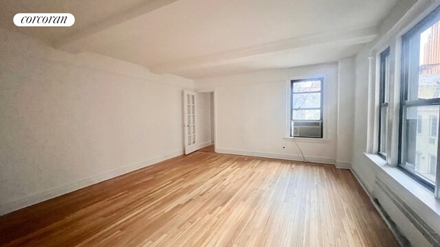 empty room with cooling unit, radiator heating unit, beam ceiling, and light hardwood / wood-style flooring