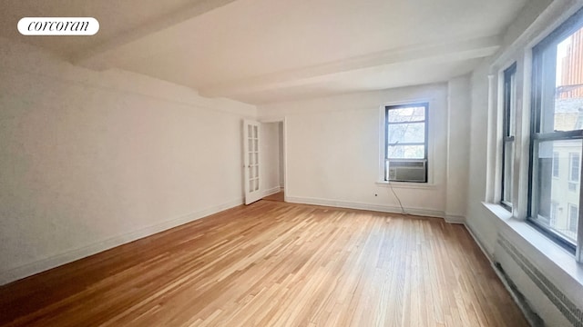 empty room with cooling unit, visible vents, baseboards, beam ceiling, and light wood finished floors