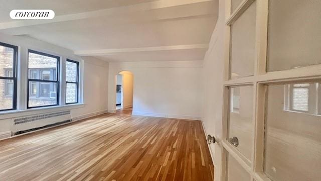 319 E 50th St Unit 5G, New York City, NY 10022 - spare room featuring radiator, arched walkways, wood finished floors, and beamed ceiling