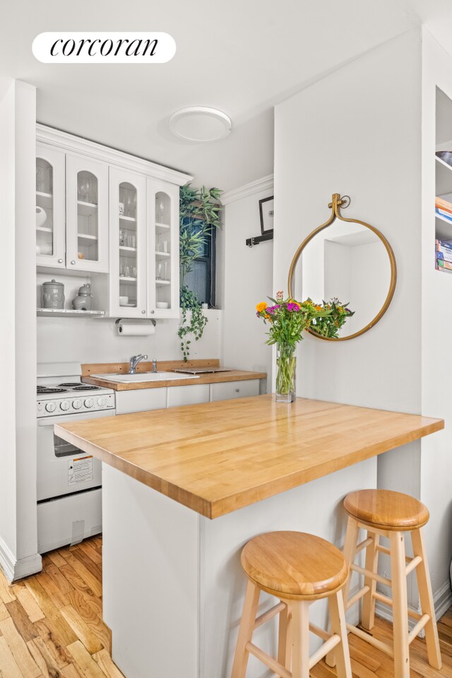 kitchen featuring electric range, butcher block countertops, white cabinets, and a breakfast bar area