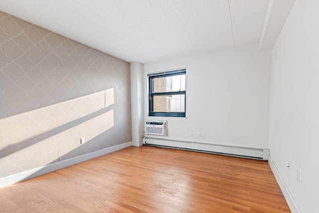 empty room with a wall mounted air conditioner, wood finished floors, wallpapered walls, a baseboard radiator, and an accent wall