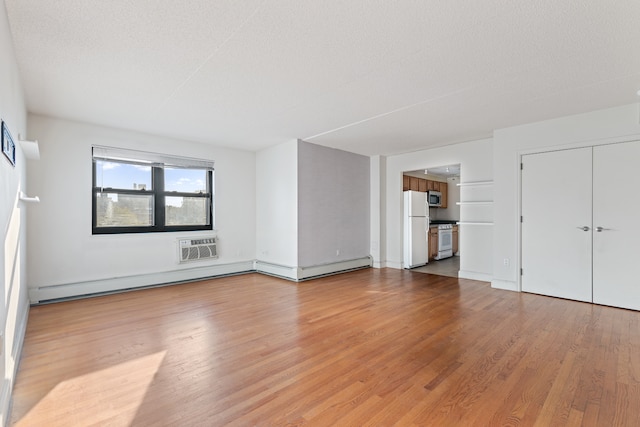 unfurnished bedroom featuring a wall unit AC, light wood-type flooring, freestanding refrigerator, and a textured ceiling