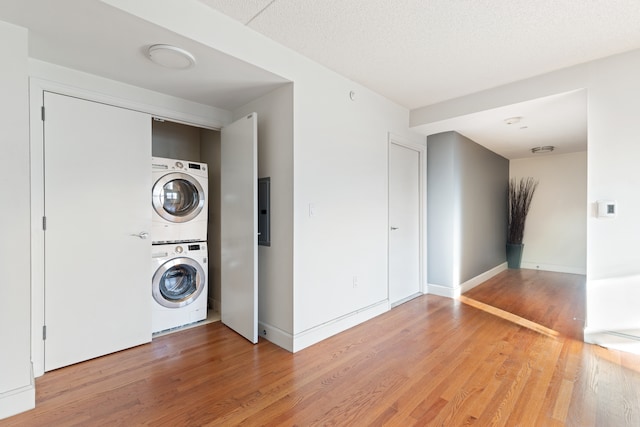 washroom featuring light wood-style flooring, electric panel, stacked washing maching and dryer, baseboards, and laundry area