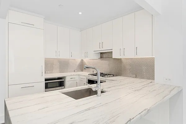 kitchen with a sink, light stone counters, backsplash, and appliances with stainless steel finishes