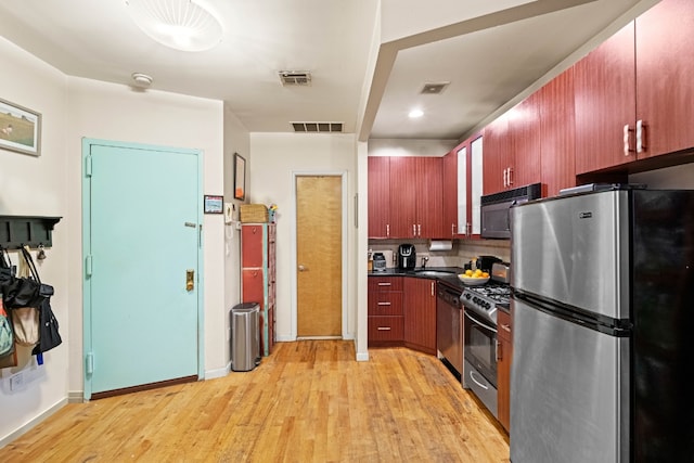 kitchen with light wood-type flooring, stainless steel appliances, backsplash, and sink