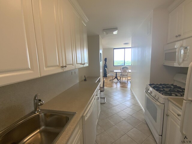 kitchen with white cabinets, light tile patterned floors, sink, and white appliances