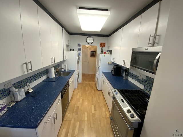 kitchen with dark countertops, decorative backsplash, appliances with stainless steel finishes, and light wood-style floors