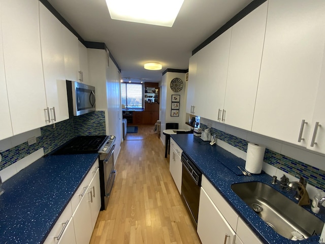 kitchen featuring white cabinetry, a sink, stainless steel appliances, light wood finished floors, and backsplash