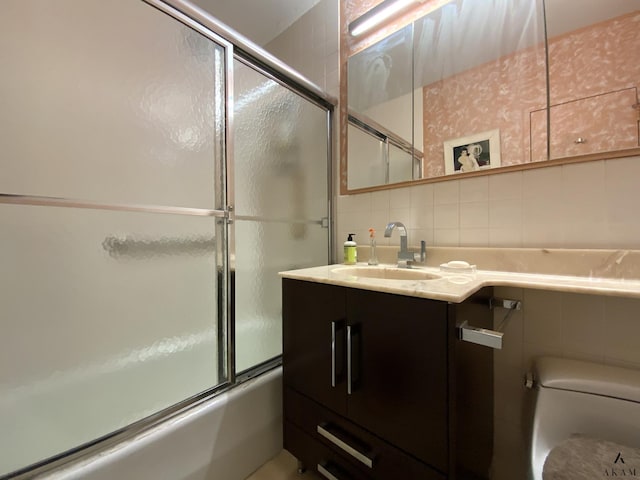 bathroom with tile walls, vanity, toilet, bath / shower combo with glass door, and backsplash