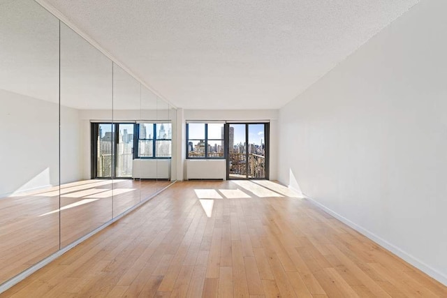 empty room with light wood-type flooring, baseboards, a city view, and a textured ceiling