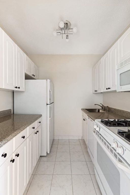 kitchen featuring white cabinetry, white appliances, sink, and dark stone countertops