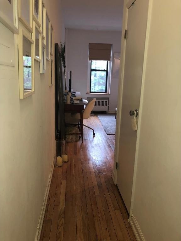 hallway with dark wood finished floors, radiator heating unit, and baseboards