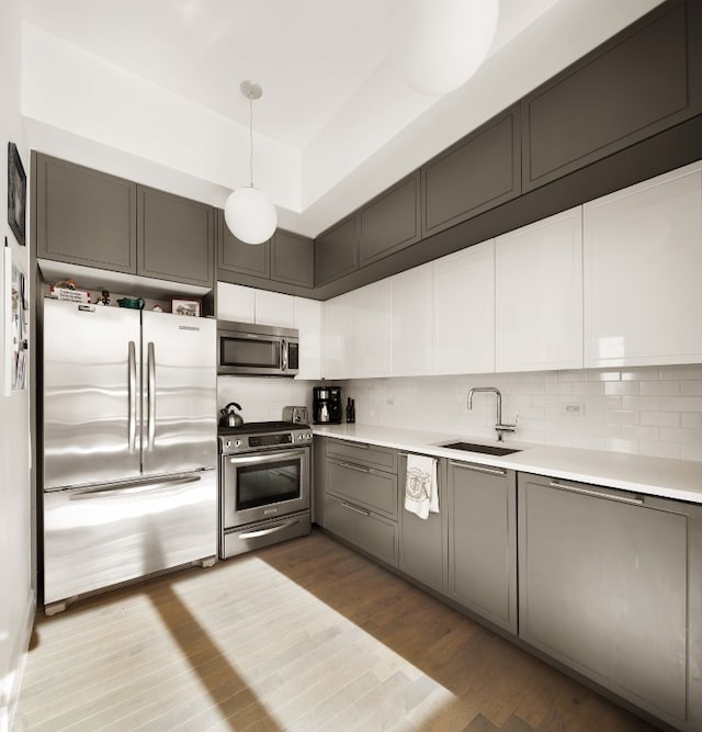 kitchen with pendant lighting, sink, hardwood / wood-style flooring, appliances with stainless steel finishes, and tasteful backsplash