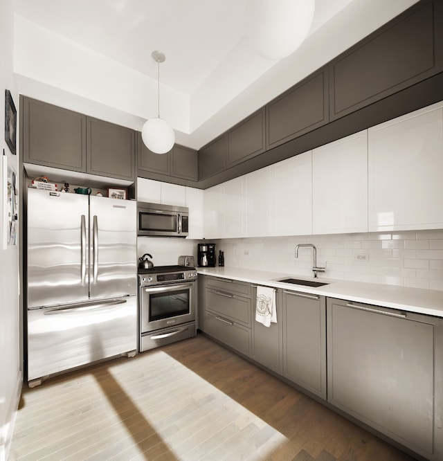 kitchen with a sink, appliances with stainless steel finishes, backsplash, and wood finished floors