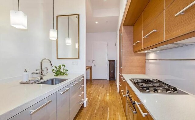 kitchen featuring sink, stainless steel gas cooktop, pendant lighting, and light hardwood / wood-style flooring