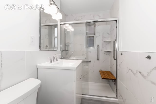 bathroom with tile walls, a marble finish shower, vanity, and toilet