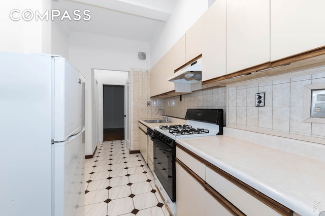 kitchen with light countertops, freestanding refrigerator, a sink, gas range, and under cabinet range hood