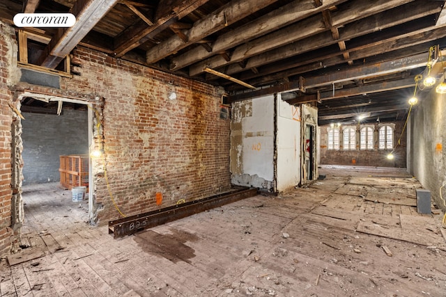 misc room featuring beam ceiling and brick wall