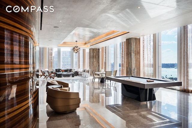 interior space with a wall of windows, a tray ceiling, a chandelier, and pool table