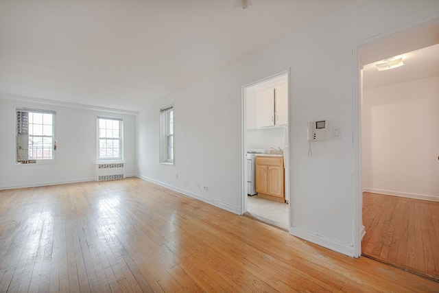 unfurnished living room with radiator, washer / dryer, and light wood-type flooring