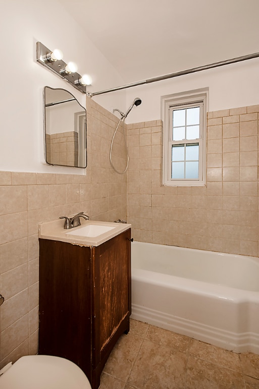 full bathroom featuring tile walls, tile patterned flooring, vanity, tiled shower / bath combo, and toilet