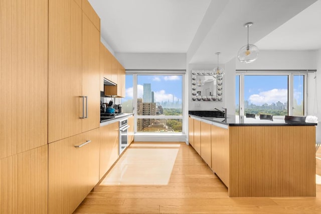 kitchen with decorative light fixtures, light brown cabinetry, oven, and light wood-type flooring