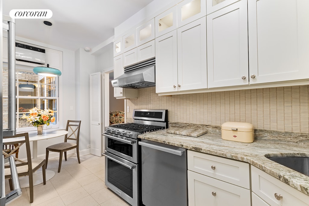 kitchen featuring appliances with stainless steel finishes, under cabinet range hood, decorative backsplash, light tile patterned floors, and white cabinetry
