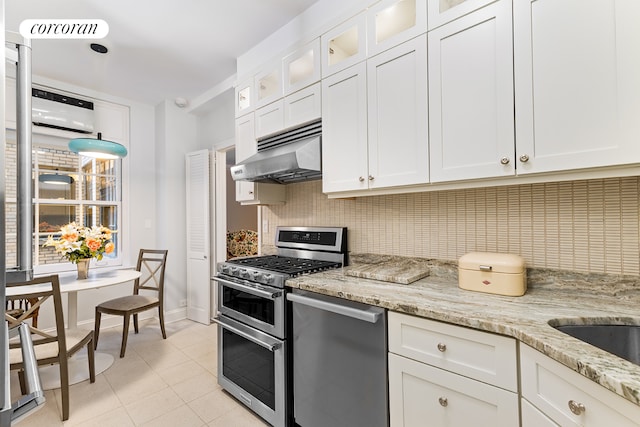 kitchen featuring appliances with stainless steel finishes, under cabinet range hood, decorative backsplash, light tile patterned floors, and white cabinetry