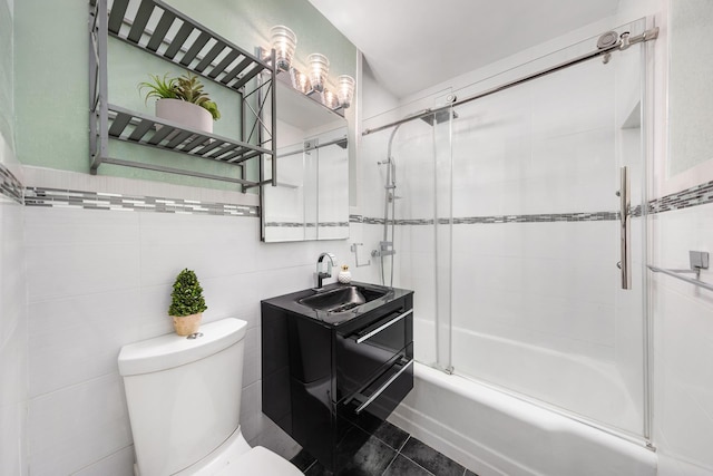 bathroom with toilet, tile patterned floors, combined bath / shower with glass door, vanity, and tile walls