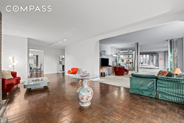 living room featuring arched walkways, rail lighting, and baseboards