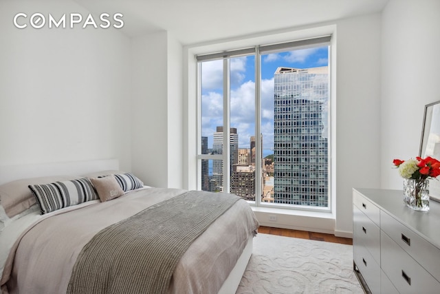 bedroom with a view of city and wood finished floors