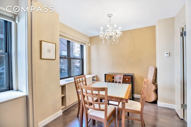 dining area featuring dark wood-type flooring, a notable chandelier, and baseboards