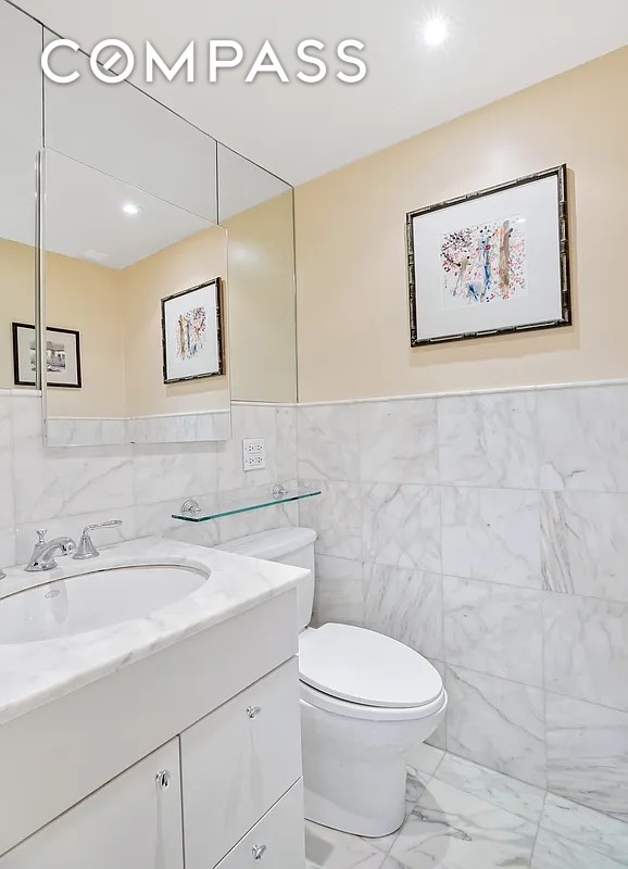50 Sutton Pl S Unit 2D, New York City, NY 10022 - bathroom with vanity, tile walls, marble look tile flooring, and wainscoting