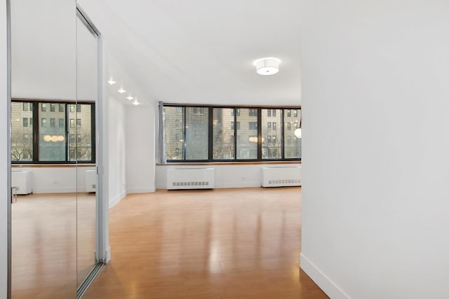 hall featuring light hardwood / wood-style flooring, radiator, and a healthy amount of sunlight