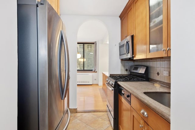 kitchen featuring light tile patterned floors, appliances with stainless steel finishes, decorative backsplash, light stone countertops, and sink