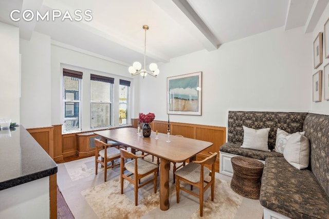 dining room with a wainscoted wall, a chandelier, and beamed ceiling