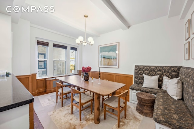 dining room featuring a wainscoted wall, a chandelier, beam ceiling, and wood walls