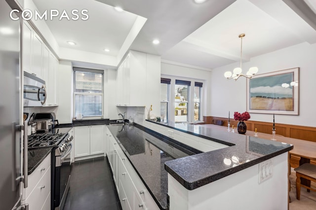 kitchen featuring a wainscoted wall, appliances with stainless steel finishes, white cabinets, a sink, and dark stone counters