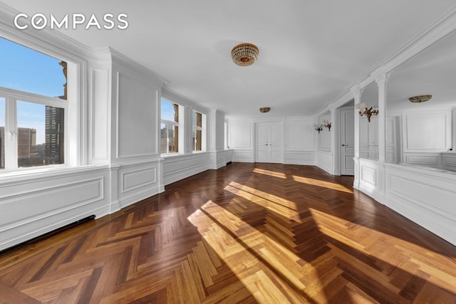 unfurnished room featuring ornate columns, a healthy amount of sunlight, and a decorative wall