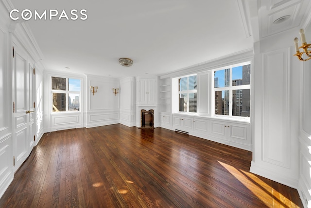 unfurnished living room featuring built in shelves, ornamental molding, a fireplace, dark wood-style floors, and a decorative wall