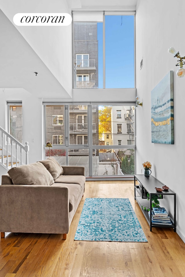 living area featuring stairs, a wall of windows, a high ceiling, and wood finished floors