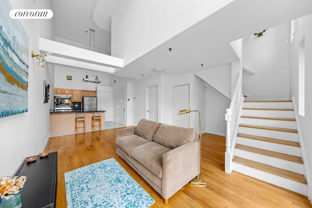 living room with light wood-style floors, stairway, a towering ceiling, and baseboards