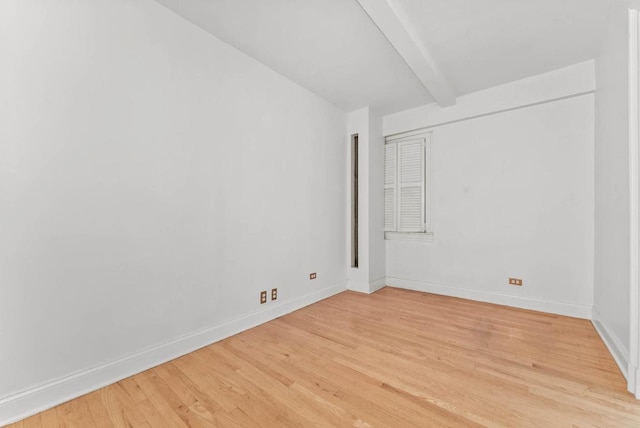 spare room featuring light wood-style flooring, baseboards, and beam ceiling