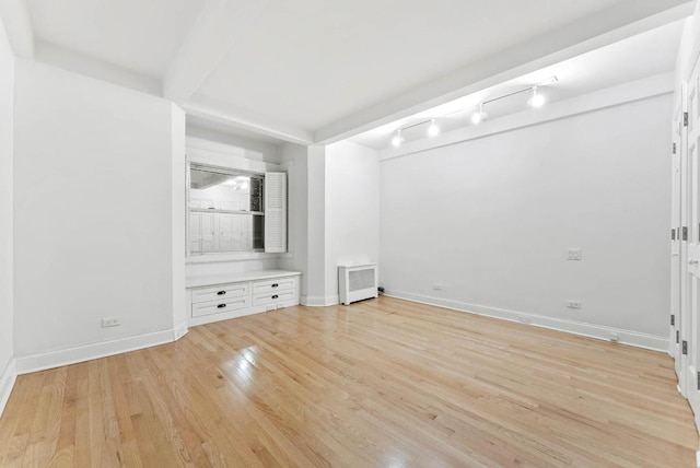 unfurnished bedroom with beam ceiling, light wood-type flooring, radiator, and baseboards