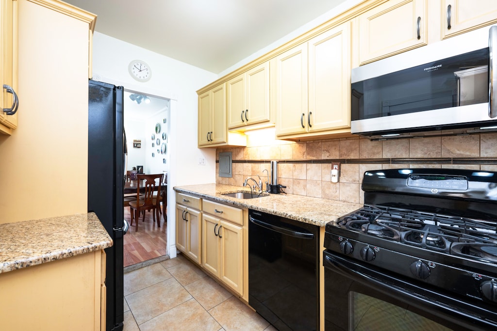 kitchen with light tile patterned floors, a sink, cream cabinetry, decorative backsplash, and black appliances