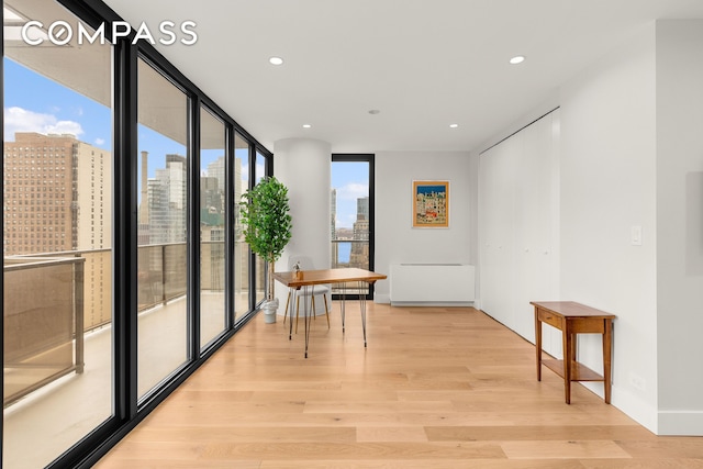 interior space with baseboards, light wood-style flooring, a view of city, expansive windows, and recessed lighting